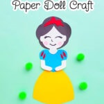 pretty Disney princess Snow White paper doll on a green background with four green pom poms nearby