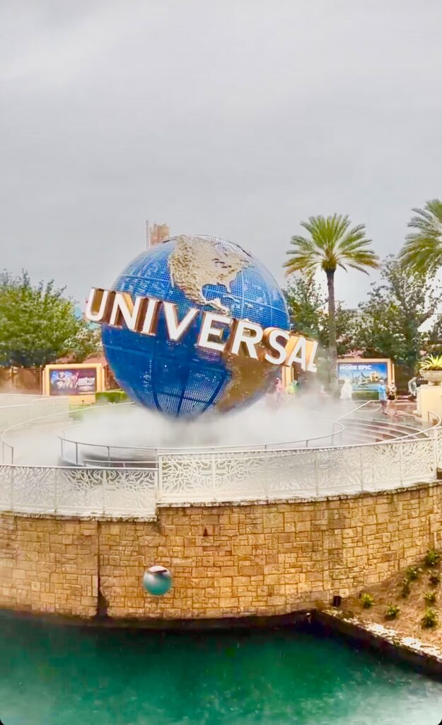 Universal globe outside of theme park entrance surrounded by lake and smoke