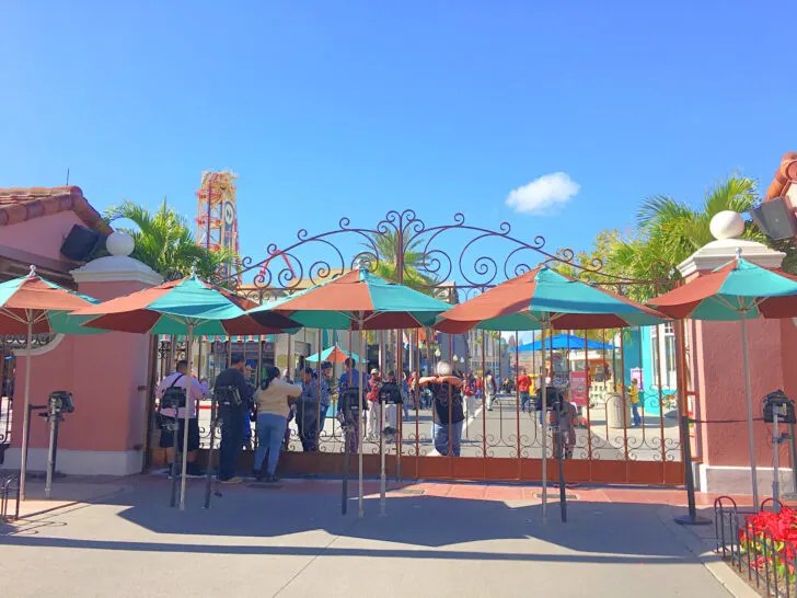 people standing by wrought iron entrance gates to Universal Studios theme park with blue sky in background