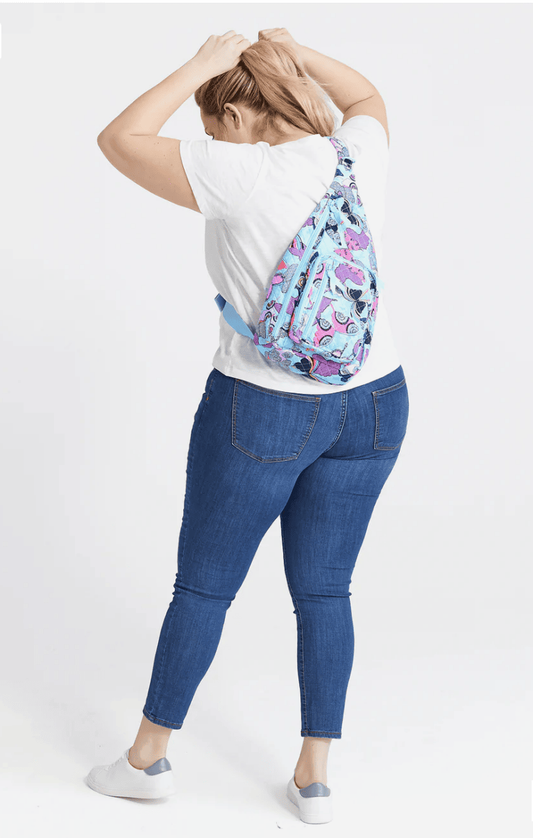 woman wearing white shirt and blue jeans with a colorful sling backpack on her back