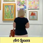woman wearing black shirt and pink skirt staring at colorful paintings on wall in art gallery
