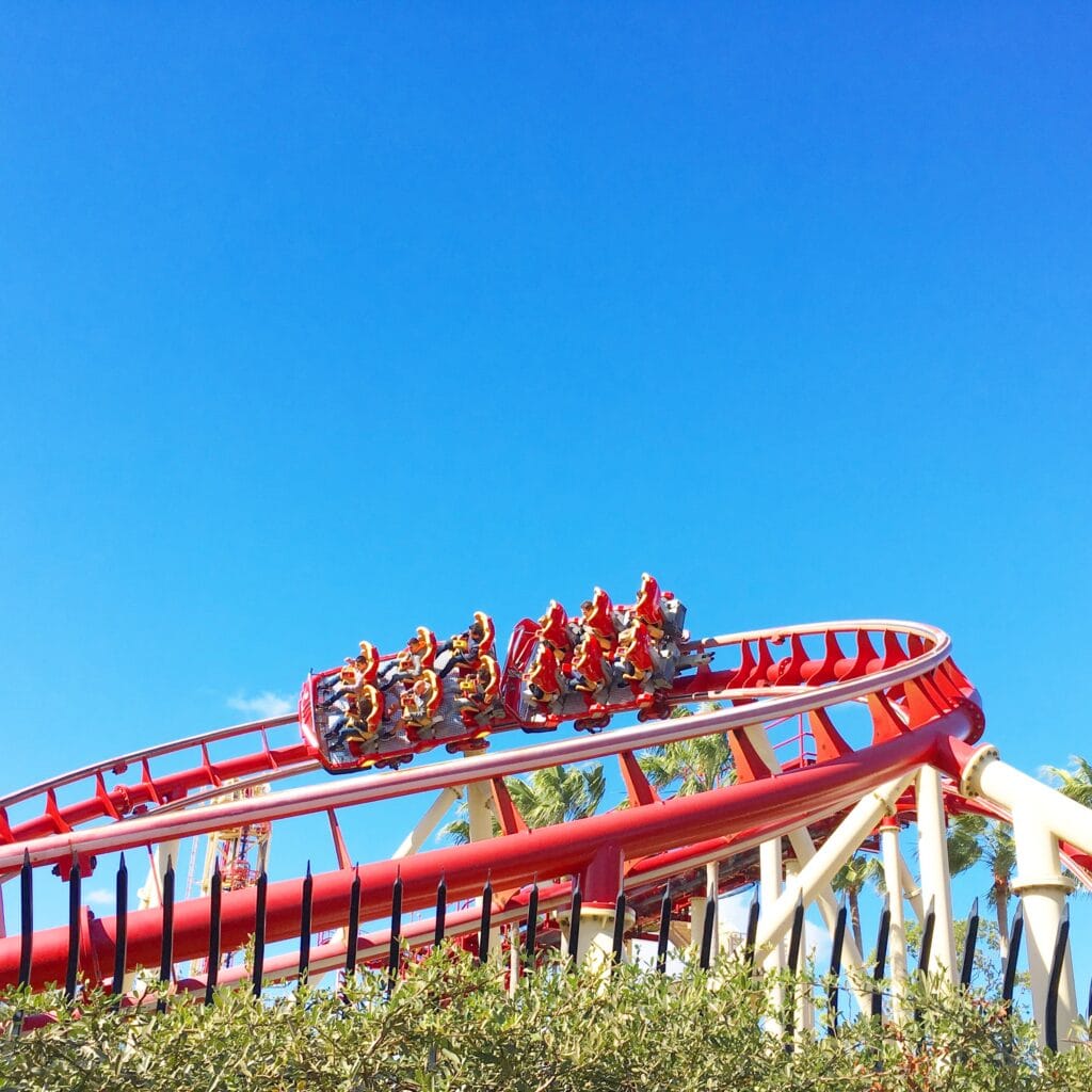 people in a roller coaster car moving along a curved red track with blue sky in background