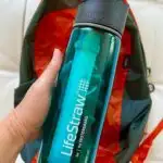hand holding a lifestraw water bottle over an orange backpack