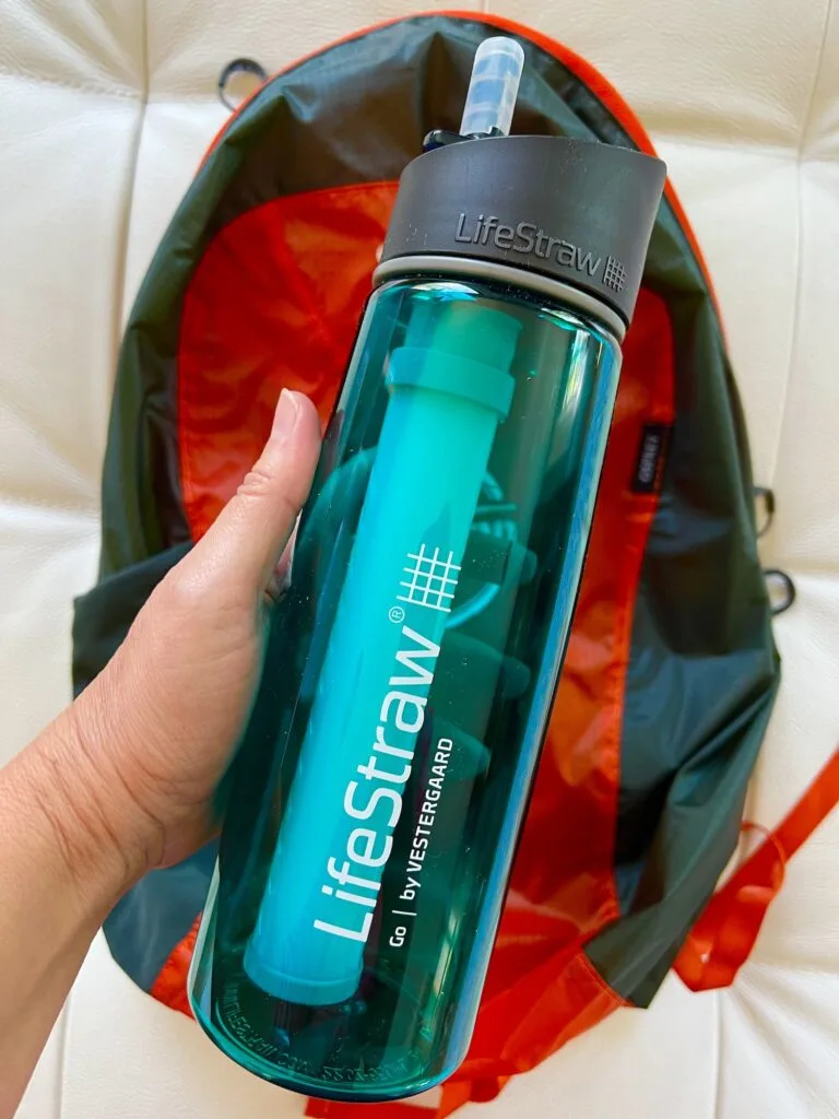 hand holding a lifestraw water bottle over an orange backpack