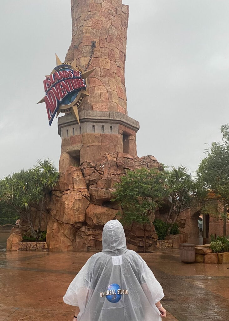 person wearing a plastic rain poncho standing outside of Islands of Adventure theme park entrance with tower in background