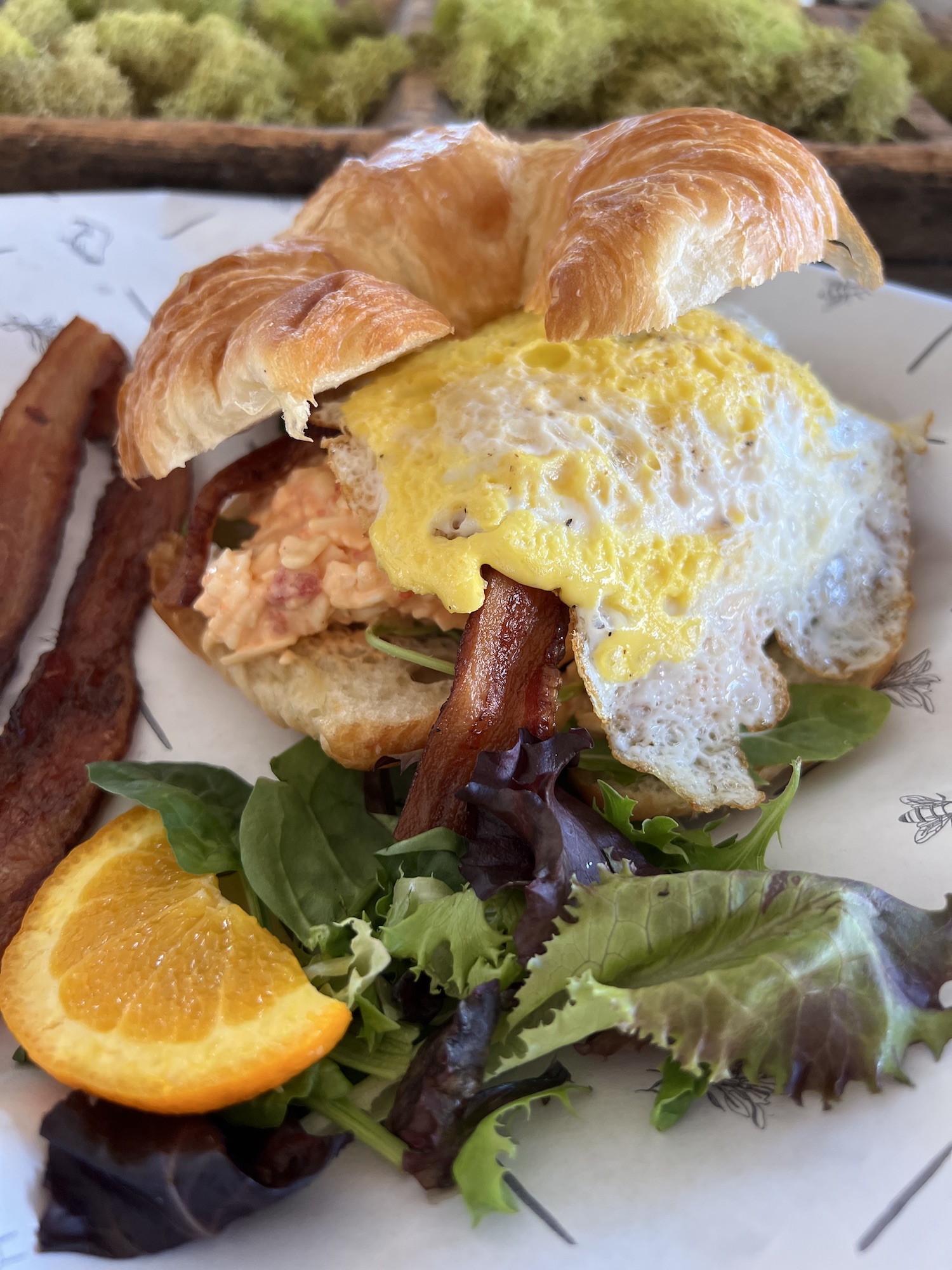 pimento cheese and fried egg on a croissant with orange slice and salad on plate nearby